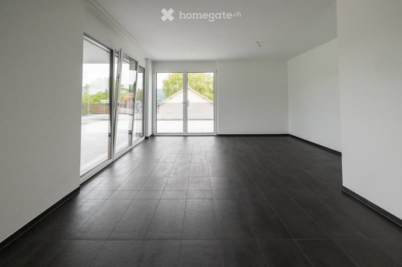 Empty room with dark tiled flooring and white walls, featuring large glass doors leading outside.