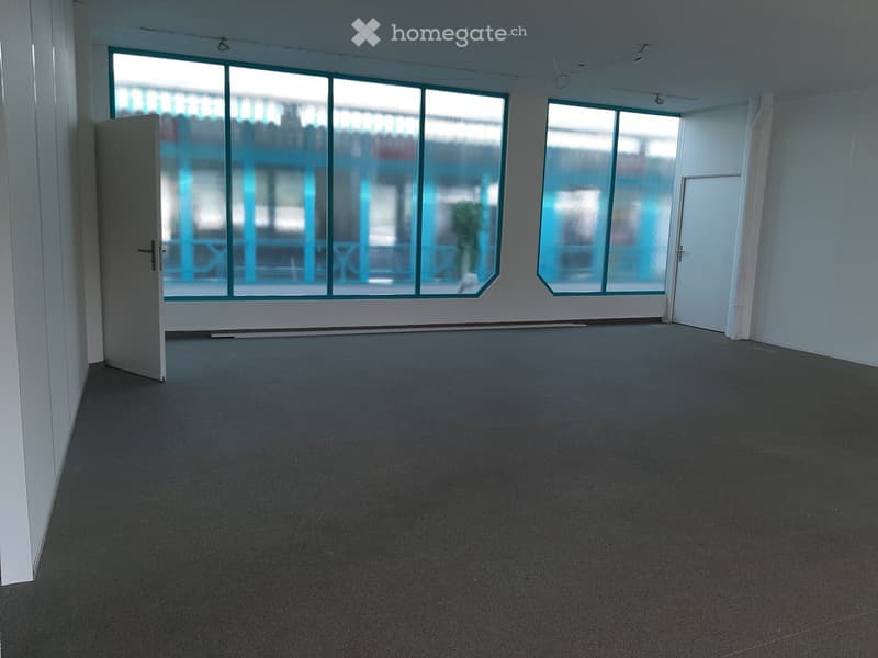 Empty room with grey carpeted floor, white walls, large windows, and a door.