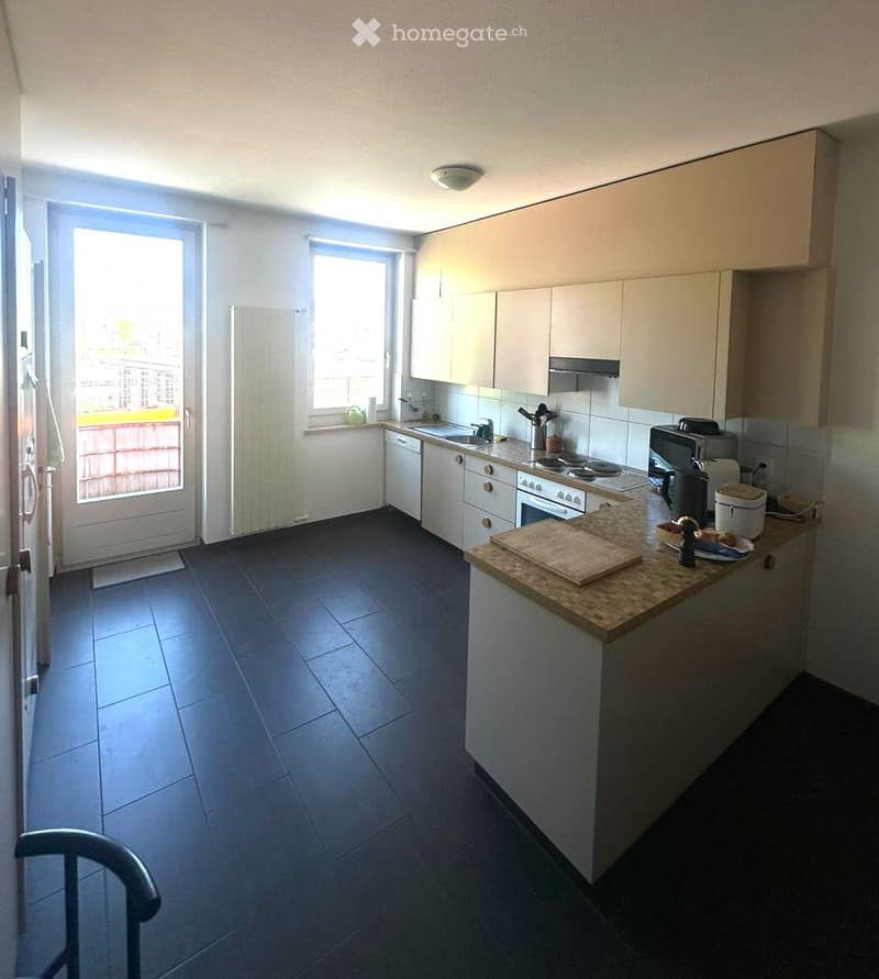 Modern kitchen with white cabinets, dark tiled floor, and various appliances including a refrigerator, dishwasher, oven, stove, microwave, and toaster. A wooden cutting board and bowl are on the counter.