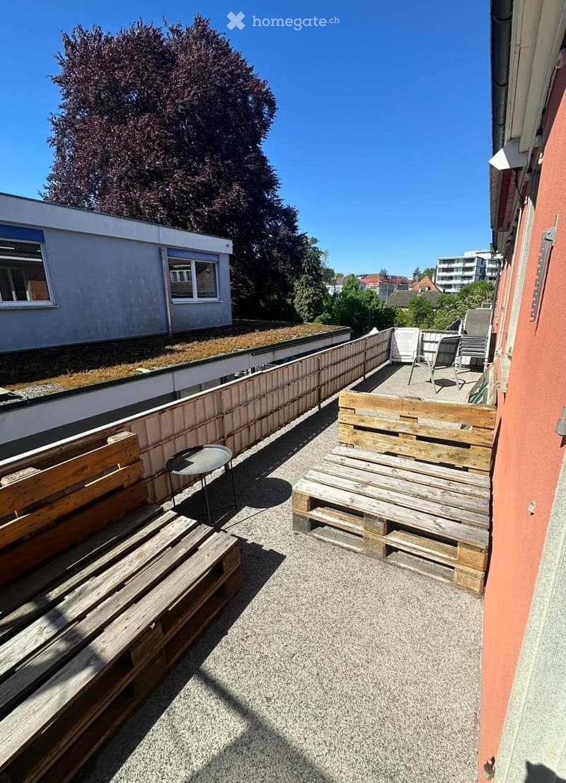 Rooftop terrace with gravel surface, wooden pallets used as seating, small round table, and chairs.