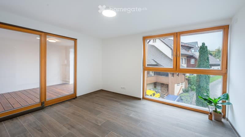 Empty room with wooden flooring, large windows, and sliding glass doors leading to a balcony area.