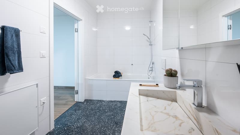Modern bathroom with white tiles, a marble sink, a bathtub, a shower, and a towel hanging on the wall.