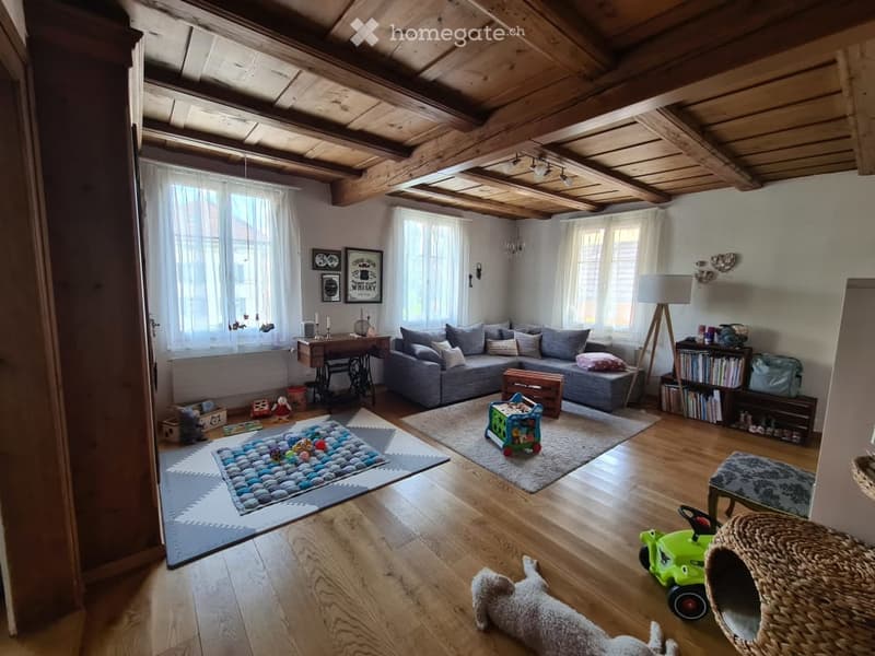 Living area with couch, two rugs, toys, wooden floor, wooden beams, white walls