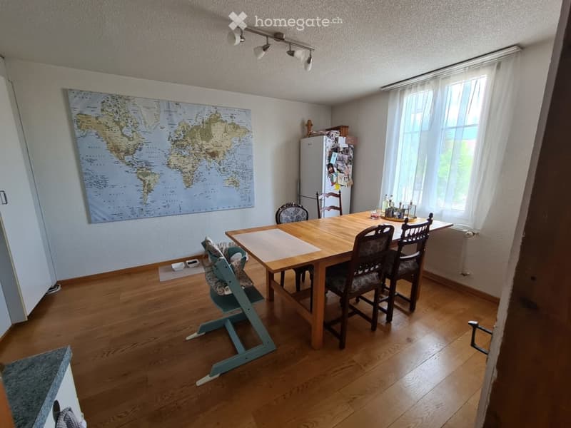 Wooden floor, large table, chairs, child's high chair, world map on the wall, refrigerator, windows, wooden ceiling lamps