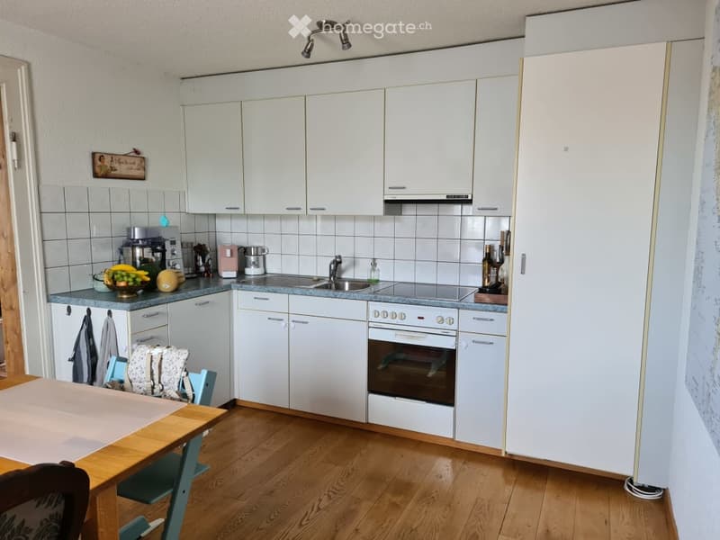 Modern kitchen with white cabinets, wooden floor, gas stove, oven, refrigerator, kitchen sink, built-in dishwasher and washing machine.