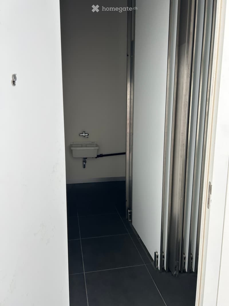 Empty room with dark tiled floor, white walls, and a small sink in the corner.