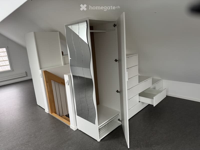 Unfurnished Room. An empty room with grey carpeted flooring and white walls. A large, modern white wardrobe with mirrored doors and multiple drawers is visible, but the room itself is unfurnished with no additional furniture or items present.