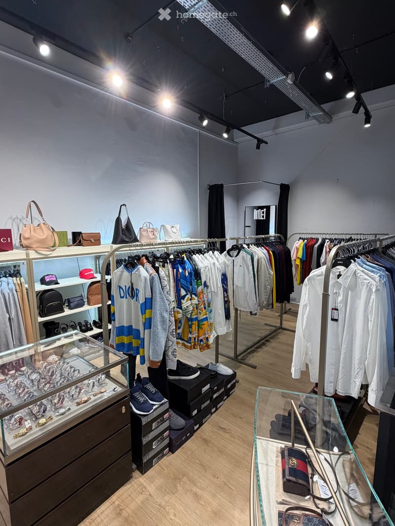 Well-lit clothing store with clothing racks, handbags, shoes, and accessories displayed on shelves and in glass cases.