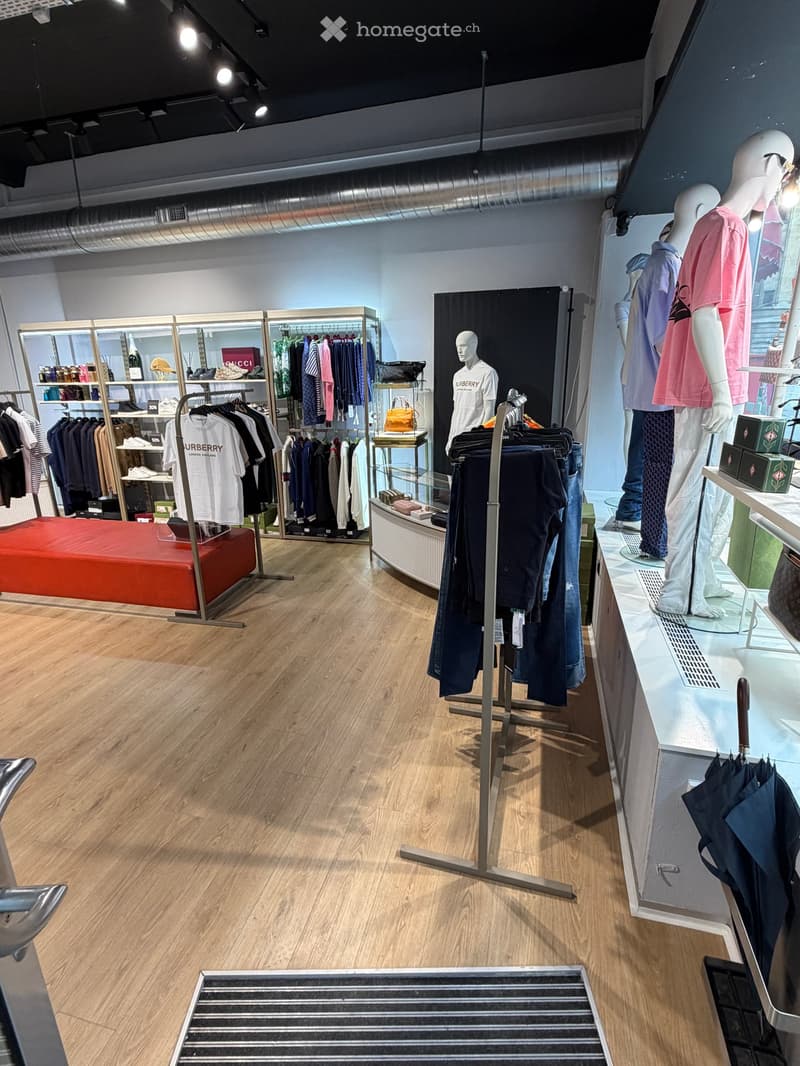 Modern retail store interior with wooden flooring, clothing racks, shelves, mannequins, handbag display, and umbrella stand.
