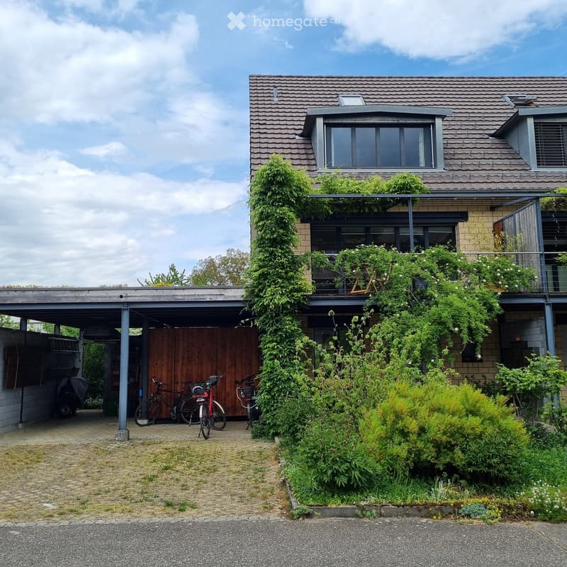 Two-story house with a tiled roof, covered garage, and balcony with greenery. Bicycles are parked under the garage.