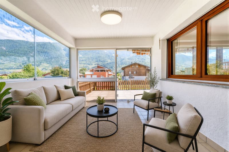 Modern living room with large windows offering a scenic mountain view, featuring a beige sofa, armchairs, a coffee table, and potted plants.