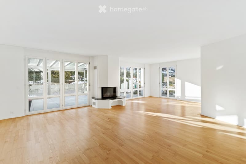 Bright, empty room with light wooden flooring and white walls, featuring large glass doors leading to an outdoor area.