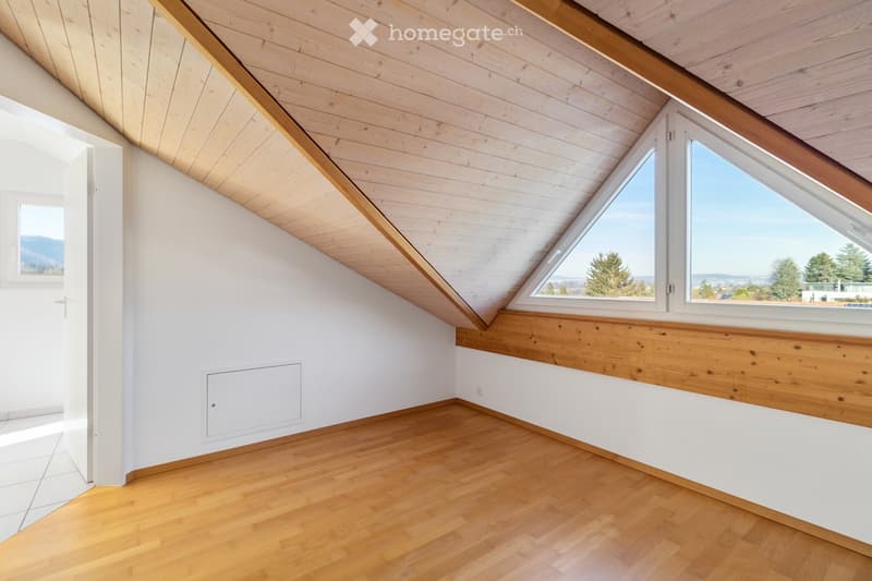 Bright, empty attic room with wooden floors, white walls, and large skylight windows offering a scenic view.