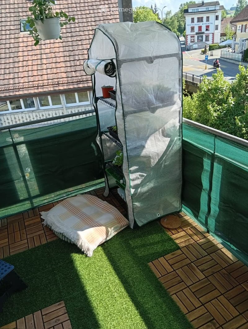 Balcony with wooden decking, artificial grass, cushion, and a covered seating area with a fan.