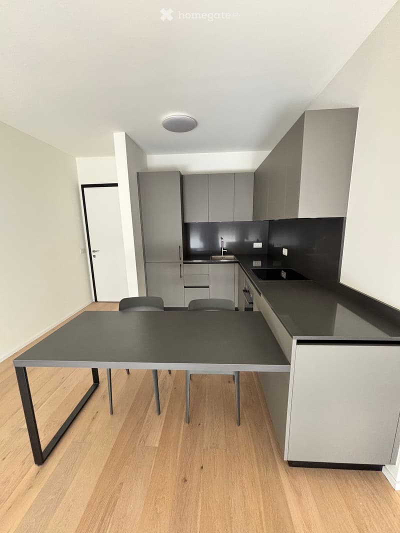 Modern kitchen with grey cabinets, black countertops, a dining table with chairs, and a sink area.