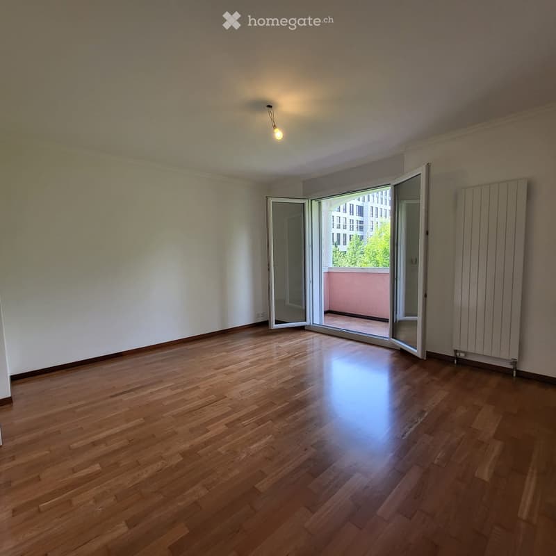 Empty room with wooden flooring, white walls, and a large open sliding door leading to a balcony.