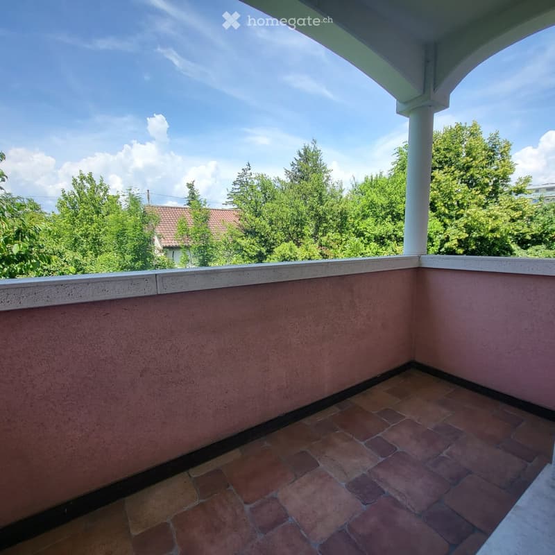 Balcony with tiled floor, low railing, and view of trees and a house in the background.
