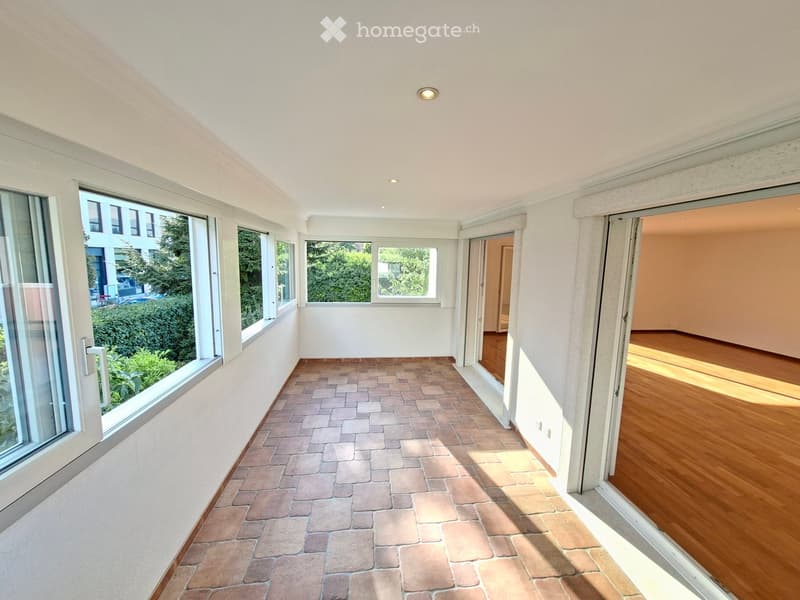 Empty hallway with tiled floor, large windows, and open doors leading to adjacent rooms.