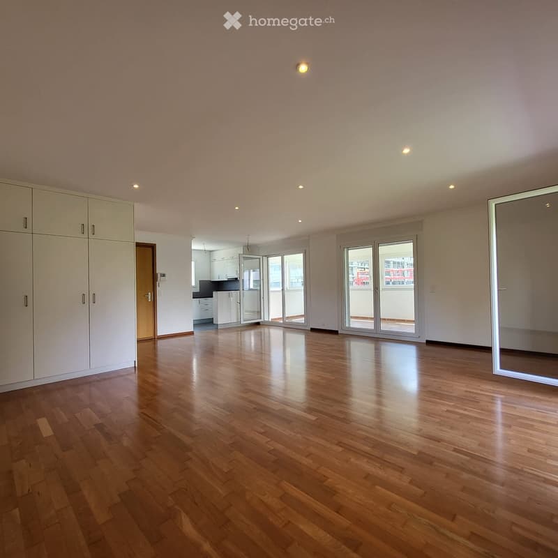Empty room with wooden flooring, white walls, and large sliding glass doors leading to a balcony. A built-in wardrobe is visible on the left side.