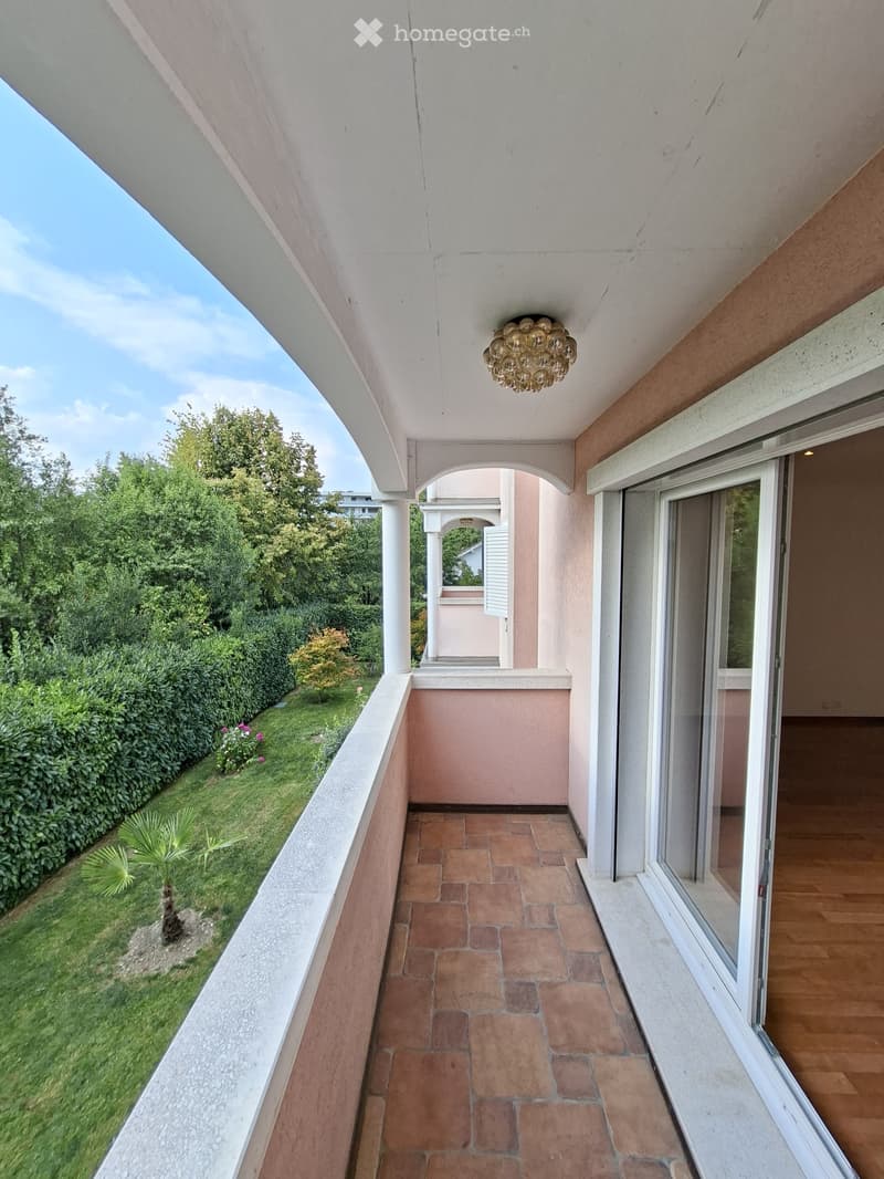 Balcony with a view of a landscaped garden, featuring a decorative wall sculpture and a glass roof structure.