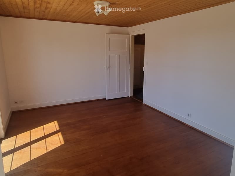 Empty room with wooden flooring, white walls, and a closed door leading to another space.