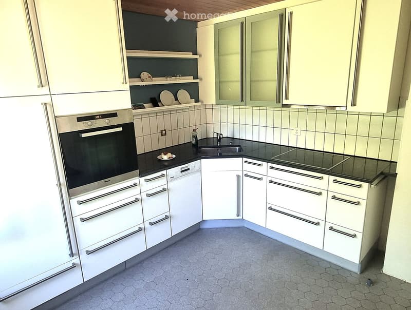 Modern kitchen with white cabinets, stainless steel appliances, black countertop, and tiled backsplash.