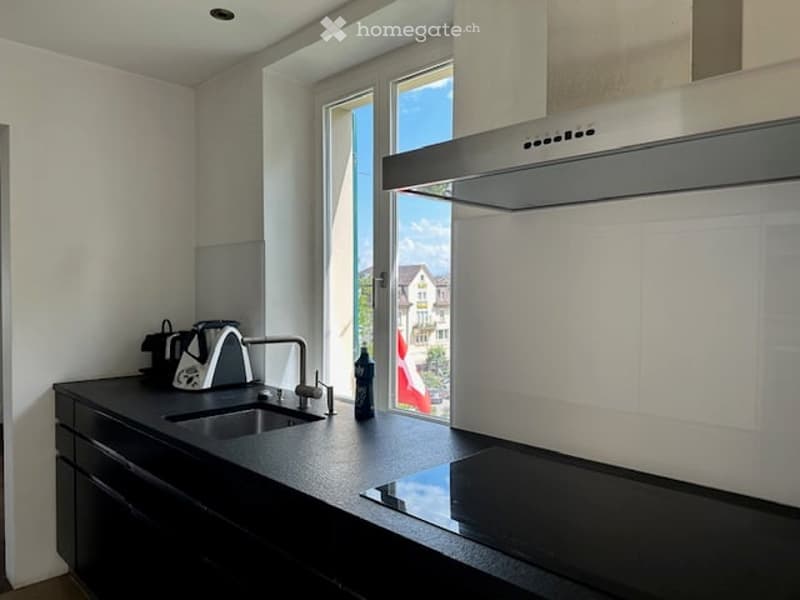modern kitchen with black countertops, stainless steel sink, induction cooktop, white walls, large window with view