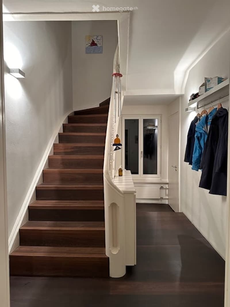 wooden stairs, white railing, white walls, wooden floor, white ceiling, clothes hanging on the wall