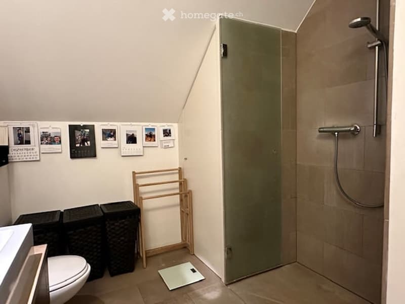 white toilet, shower, sink, wooden drying rack, storage boxes, tiled floor, tiled wall, pictures on wall