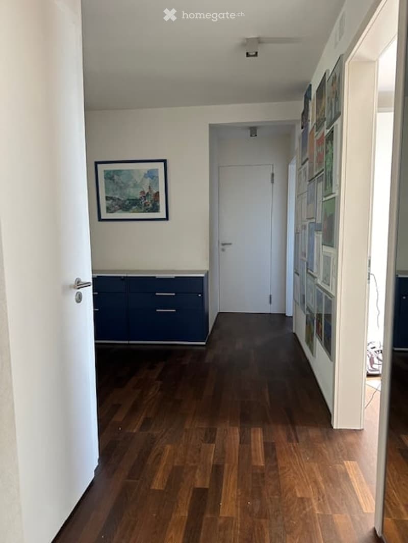 Empty hallway with wooden floor, white walls, blue cabinets, picture frame, and multiple framed pictures on the wall