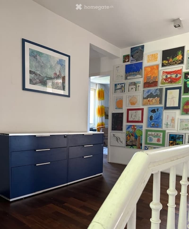 A room with a blue cabinet, a white staircase, and a wall with multiple paintings.