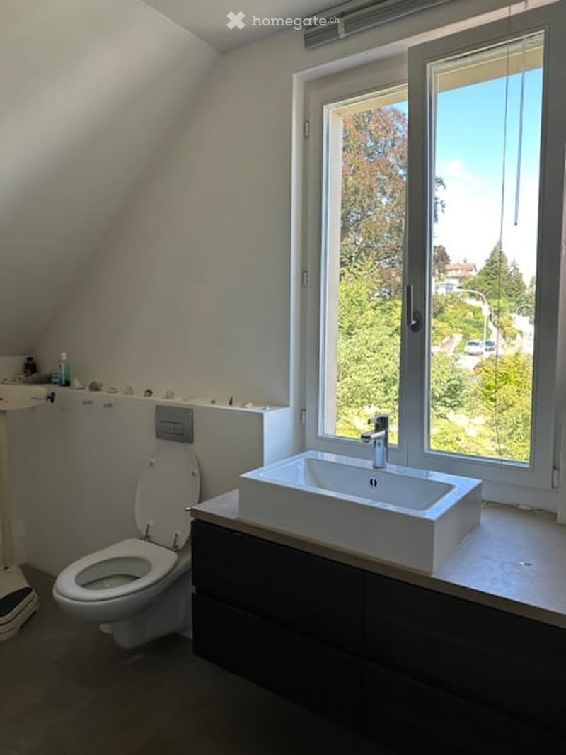 Modern bathroom with a toilet, sink, and large window offering a view of greenery outside.
