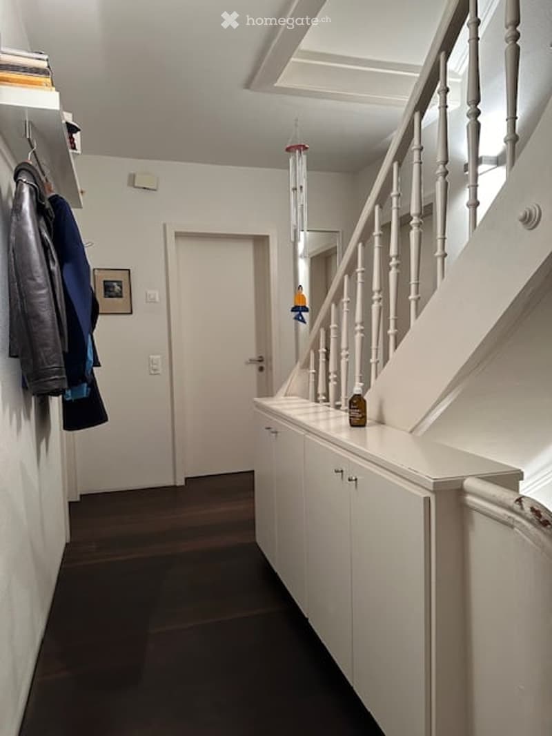 white walls, wooden floor, white cabinets, white staircase, white railings, hanging wind chime, picture frame, coat rack, power outlet, door