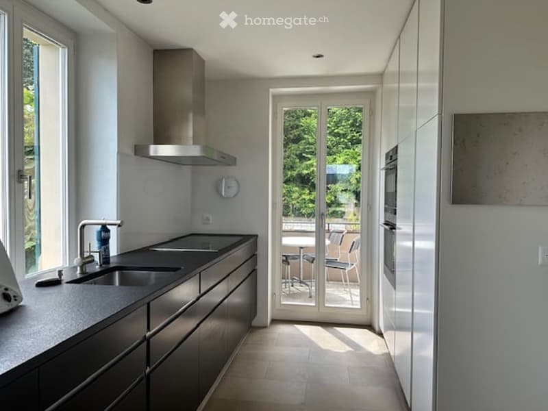 modern kitchen with black countertops, white cabinets, stainless steel appliances, double sink, sliding glass door to balcony