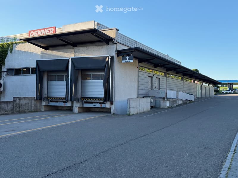 A modern industrial-style building with a large loading dock, signage reading "DENNER", and a covered entrance area.