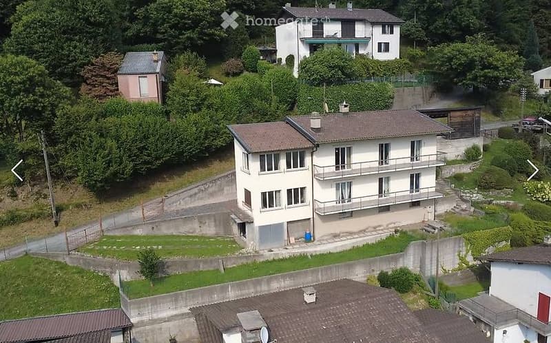 Aerial view of a multi-story residential building with balconies, surrounded by greenery and neighboring houses.