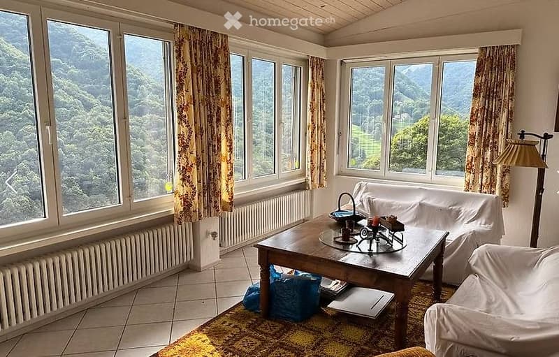 Bright living room with large windows offering a scenic mountain view, featuring a sofa, coffee table, and floor lamp.