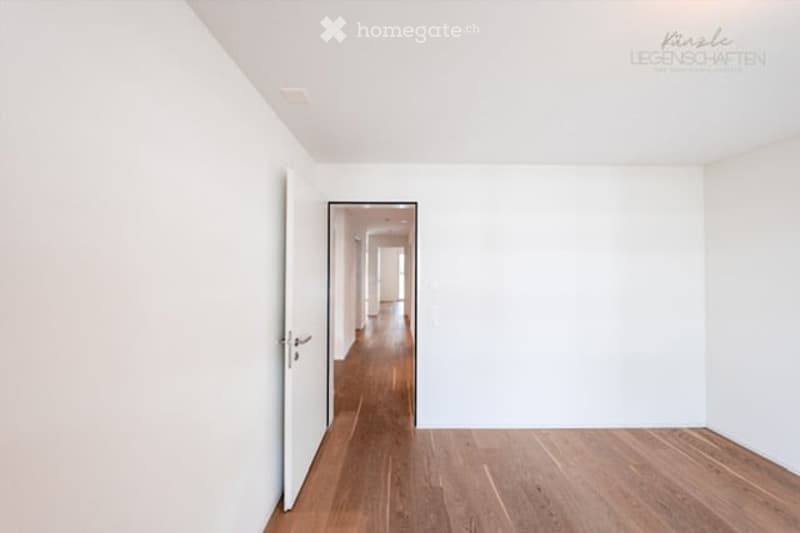 Empty room with white walls and wooden flooring, featuring an open doorway leading to a hallway.