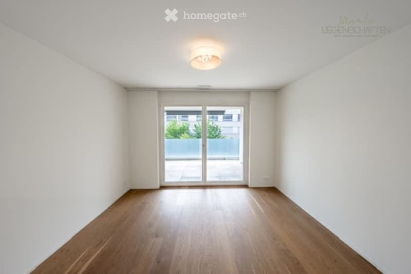 Empty room with wooden flooring, white walls, and a large glass sliding door leading to a balcony or terrace.