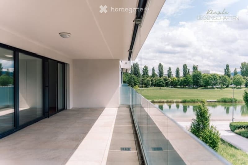 Modern balcony with large glass windows, glass railing, and scenic view of a park and water body.