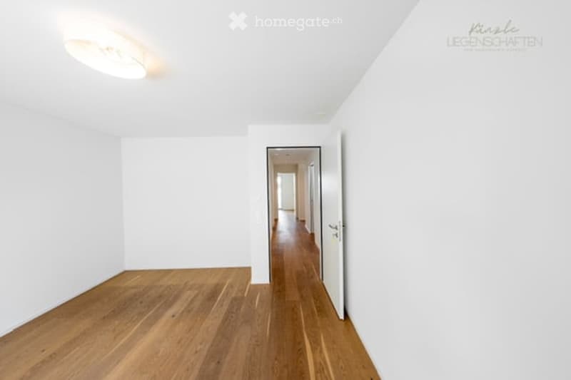 Empty room with white walls, wooden floor, and a doorway leading to a hallway.