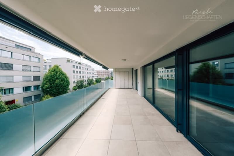 Modern balcony with large glass railings, tiled floor, and expansive city view.