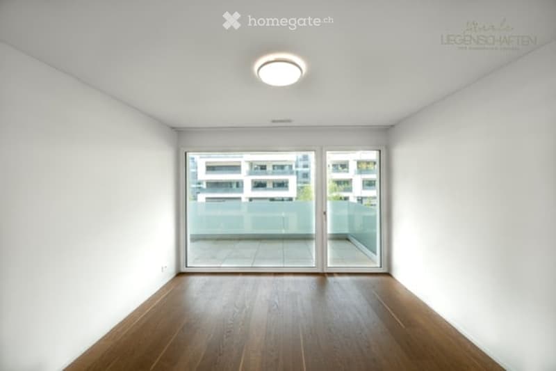 Completely empty room with white walls, wooden floor, and large glass sliding doors leading to a balcony.