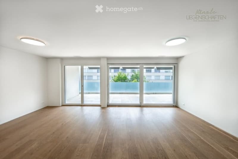 Empty room with wooden flooring, white walls, large glass sliding doors leading to a balcony, and recessed ceiling lights.