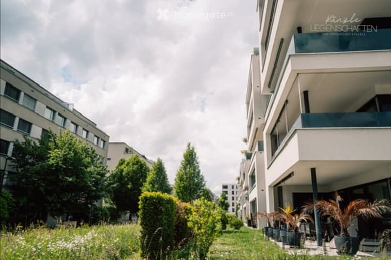 Modern residential complex with balconies, greenery, and potted plants in the foreground.