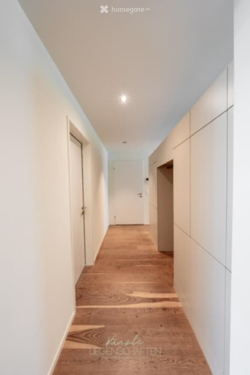 Clean, modern hallway with light wooden flooring, white walls, and built-in storage units on one side.