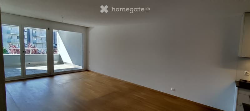 Empty room with wooden flooring, large sliding glass doors leading to a balcony, and white walls.