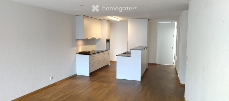 Modern kitchen with white cabinets, wooden flooring, and built-in appliances including an oven and sink.