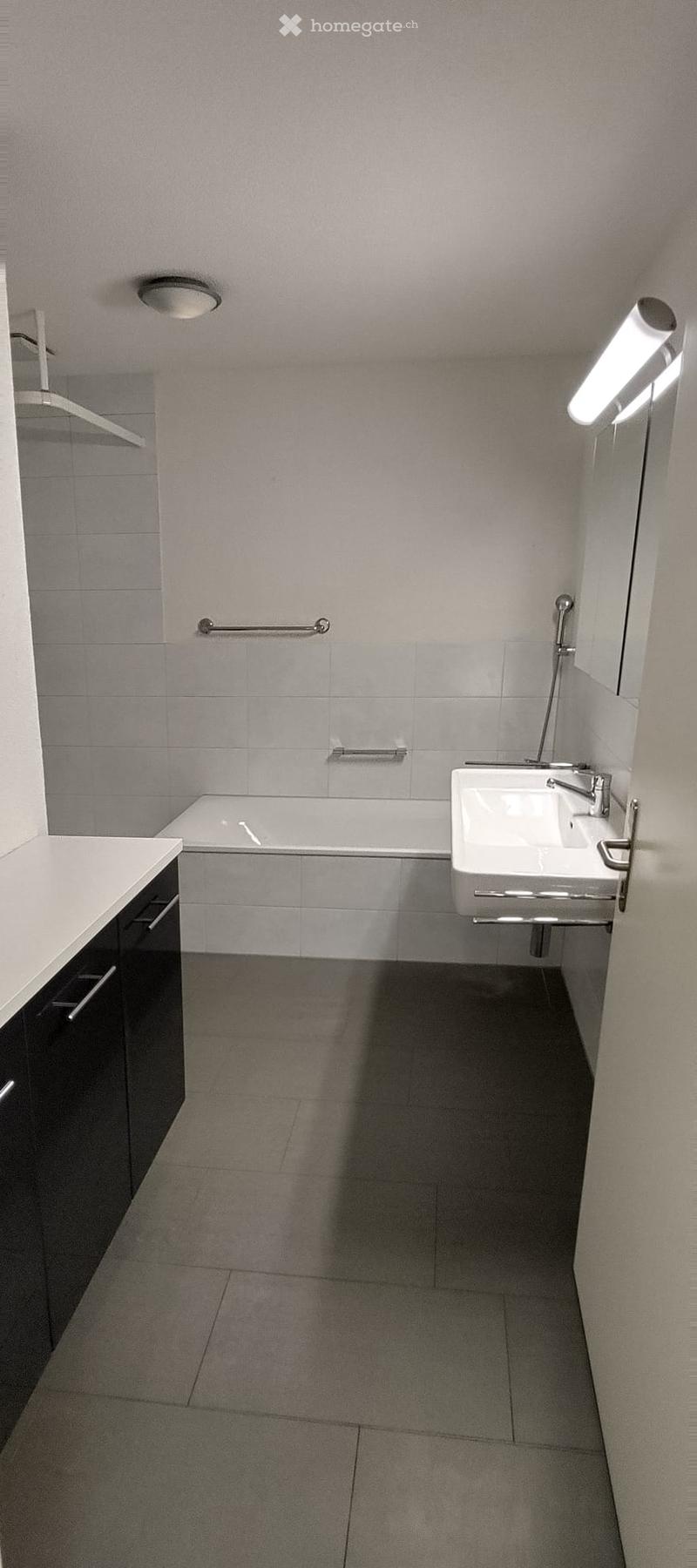 Modern bathroom with a bathtub, sink, and cabinet. Features grey tiles, a chrome faucet, and built-in storage.