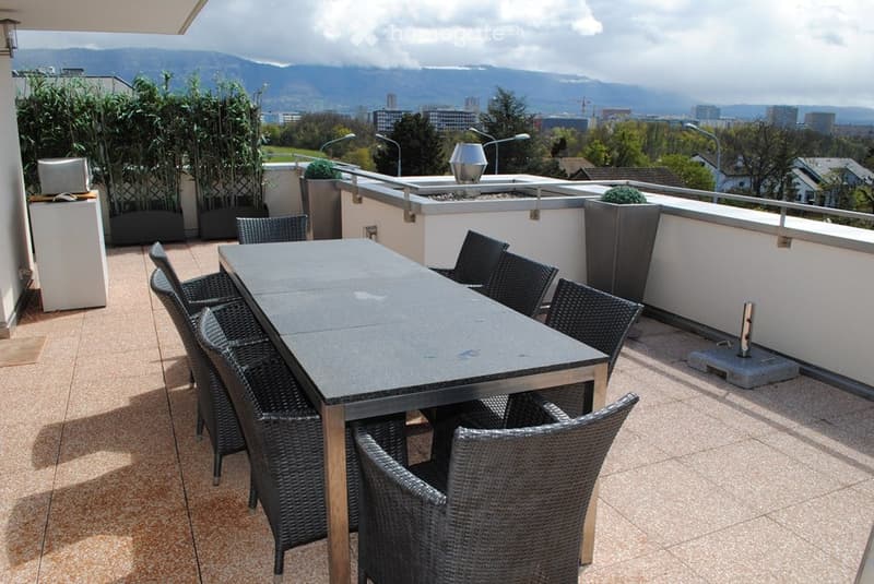 Balcony with a dining table and chairs, overlooking a cityscape with mountains in the background.